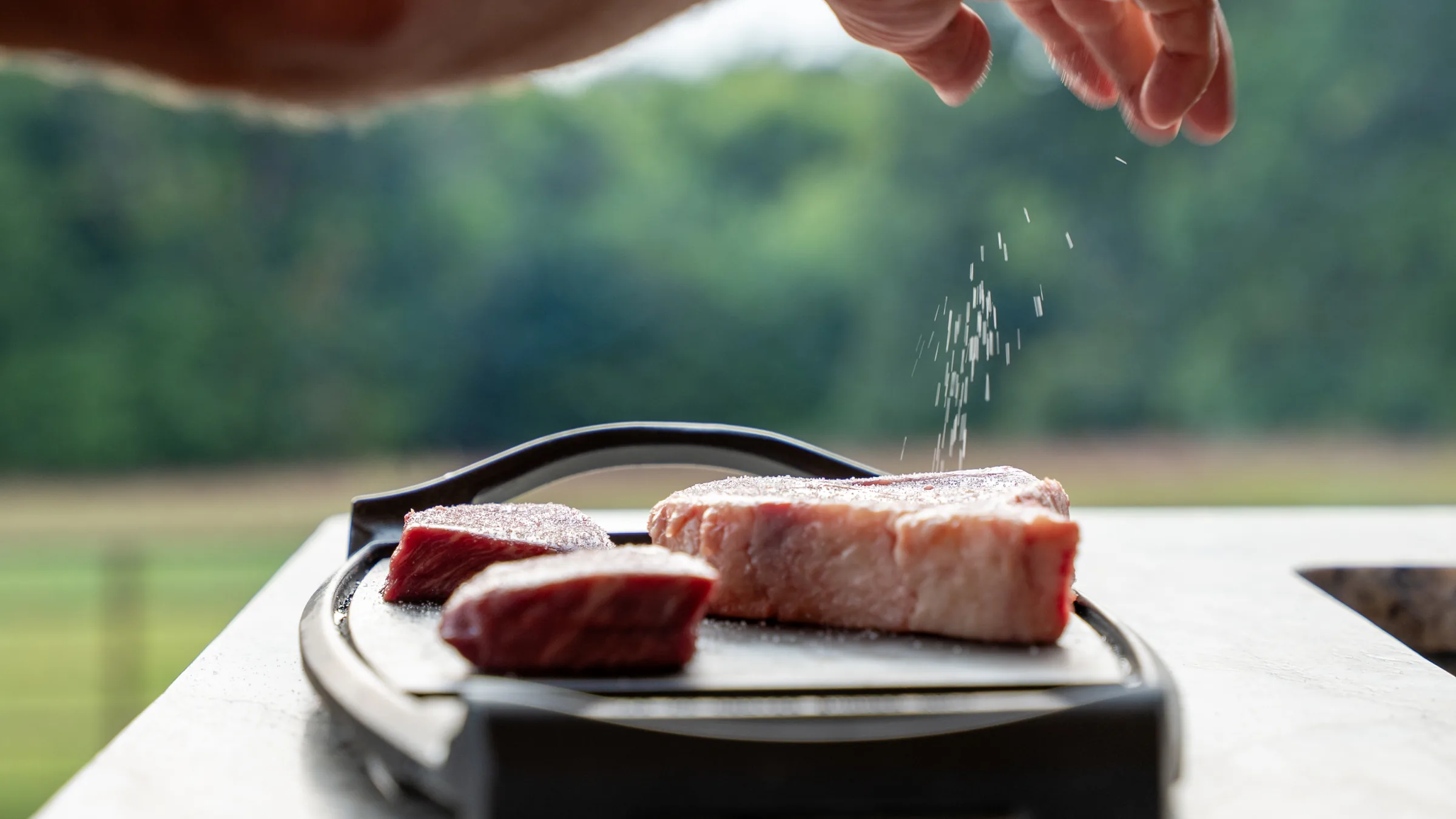 Ozark Natural Steak Co - seasoning steaks on the grill, outdoor food photography